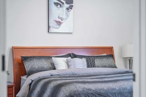 Una cama bien hecha con cabecera de madera, una mesita de noche y una lámpara de pared.