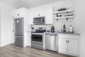 Una cocina moderna con armarios blancos, electrodomésticos de acero inoxidable, microondas, horno, lavavajillas y cafetera.
