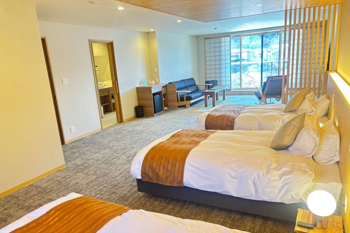 A hotel room with two beds, a desk, and a view of the outdoors.