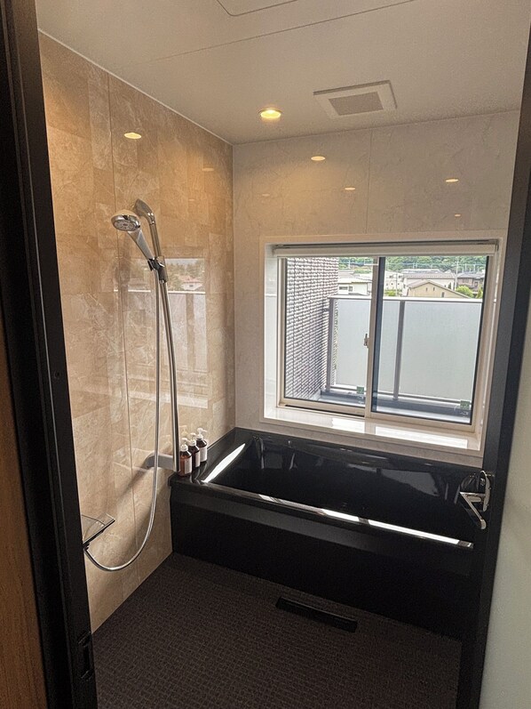 A modern bathroom with a large black bathtub, a glass-enclosed shower, and a window providing a view of the outside.