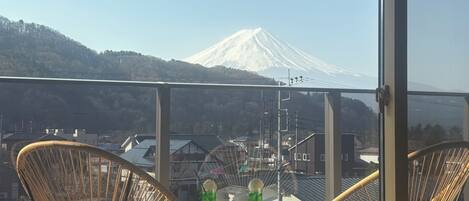 A balcony with wicker chairs and a table, overlooking a snowy mountain and buildings.