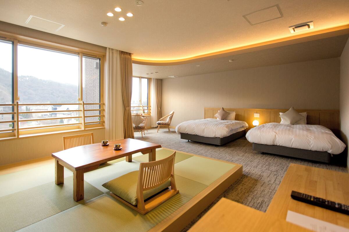 A hotel room with two beds, a dining table, and a view of the mountains.