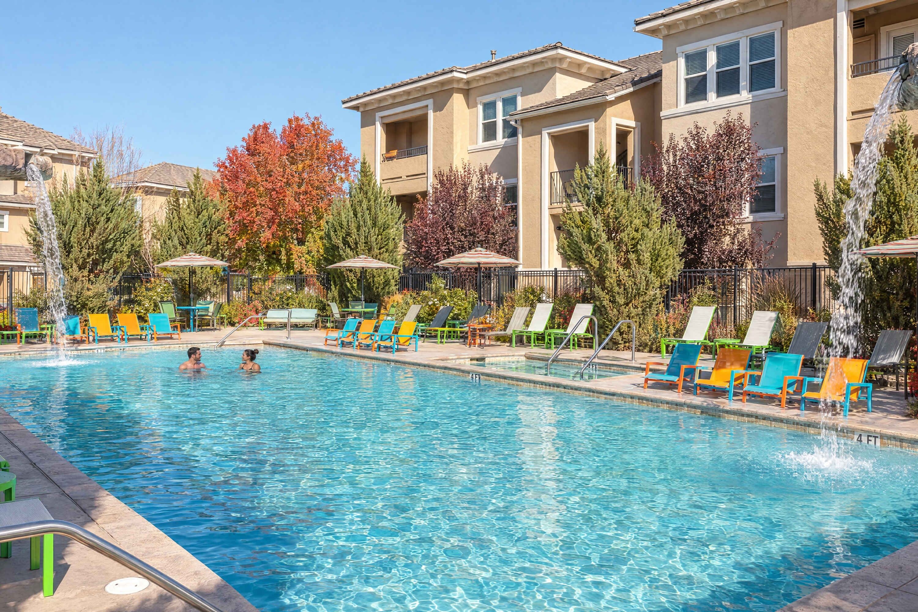 Une piscine entourée d’arbres et d’un bâtiment doté de balcons, avec plusieurs chaises longues et des parasols à proximité.