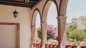 Une terrasse extérieure couverte, agrémentée d’arches en pierre, de jardinières en terre cuite ornées de fleurs et d’une lanterne suspendue.