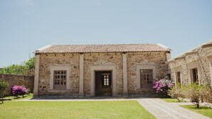 Un bâtiment en pierre avec un toit recouvert de tuiles, une porte centrale et deux fenêtres de chaque côté.