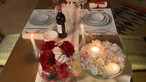 Une table à manger dressée pour quatre personnes, avec des bougies, une bouteille de vin et un vase de fleurs.