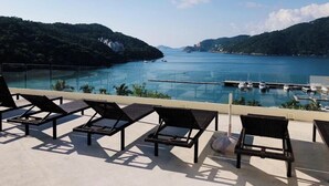 A balcony with lounge chairs overlooking a marina and a body of water. - Charming 2-bedroom apartment in gorgeous Acapulco with AC, WiFi, Ocean View (Acapulco)