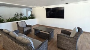 A modern outdoor living area with wicker furniture, a flat-screen TV, and a potted plant arrangement. - Charming 2-bedroom apartment in gorgeous Acapulco with AC, WiFi, Ocean View (Acapulco)