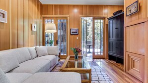 A living room with a beige sofa, a glass-top coffee table, wooden paneling, and a dark cabinet. - 11 Mi to Downtown Napa: Wine Country Cottage (Napa)