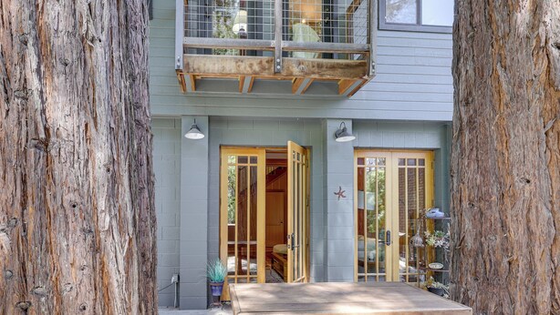 A wooden deck with a table, a building with a balcony, and a large tree trunk framing the scene. - 11 Mi to Downtown Napa: Wine Country Cottage (Napa)