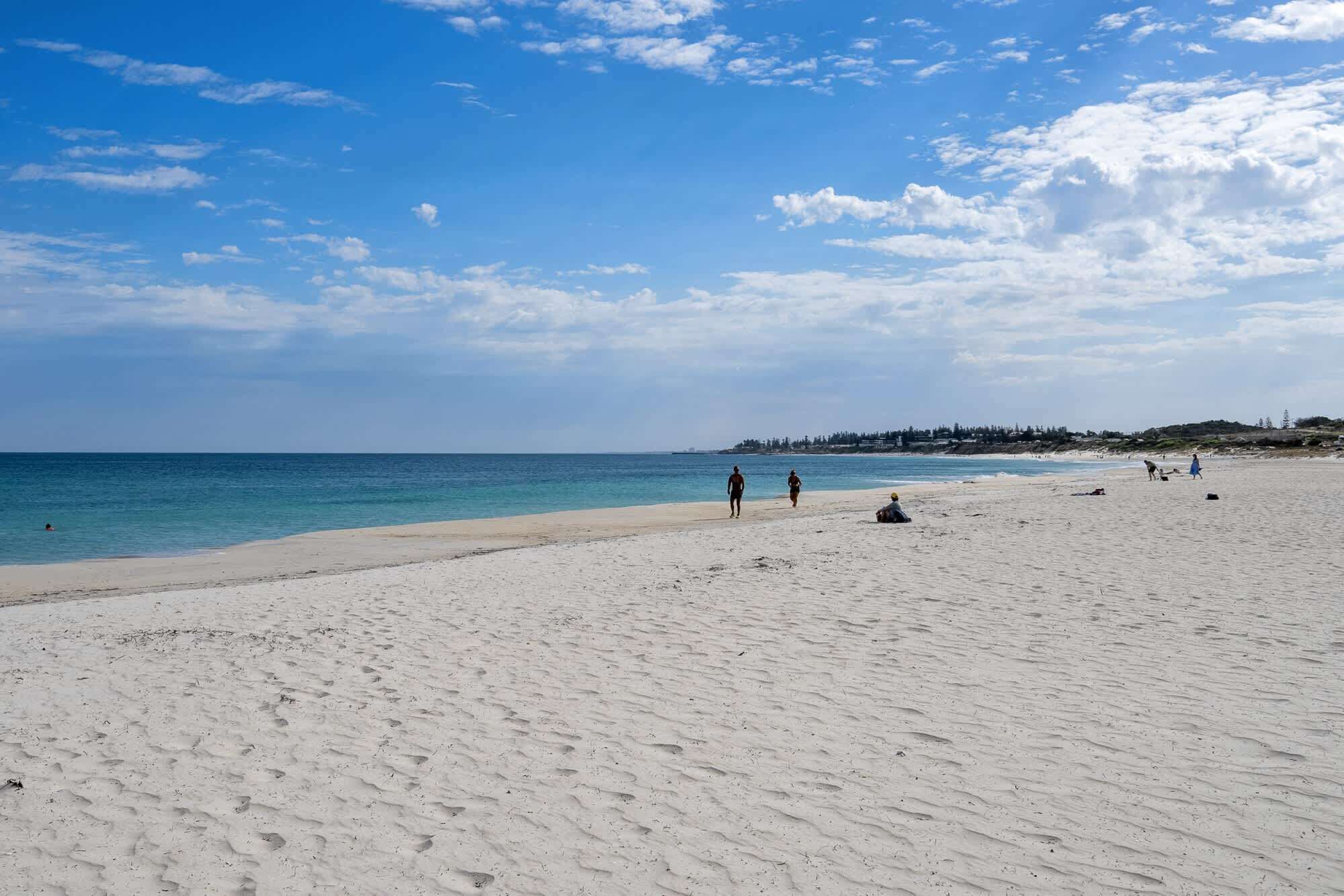 A wide sandy beach with a clear blue sky and a few people walking.