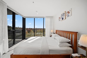 Relax in a spacious room with a large bed, sliding glass door to an outdoor area, and scenic views of trees and a bridge.