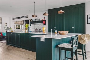 A modern kitchen with dark cabinetry, a central island, pendant lighting, and a visible kitchen sign.