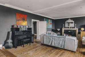 A living room with a piano, a sofa, a fireplace, and artwork on the walls.
