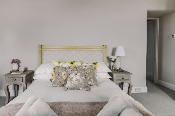 A neatly made bed with floral bedding, two bedside tables with lamps, and a door leading to another room.