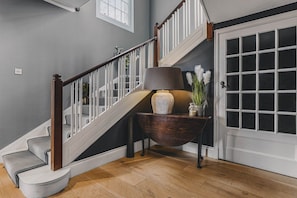 A staircase with a wooden handrail and white balusters, leading to a landing with a dark wooden console table and a vase with white flowers.