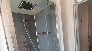 Ducha envuelta en vidrio con cabezal de ducha de mano y panel de control en la pared.