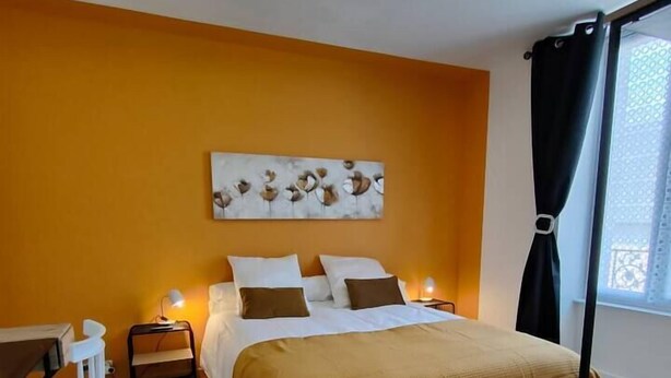 Un dormitorio con una cama, mesitas de noche, una silla, una lámpara en el techo y una ventana con cortinas.