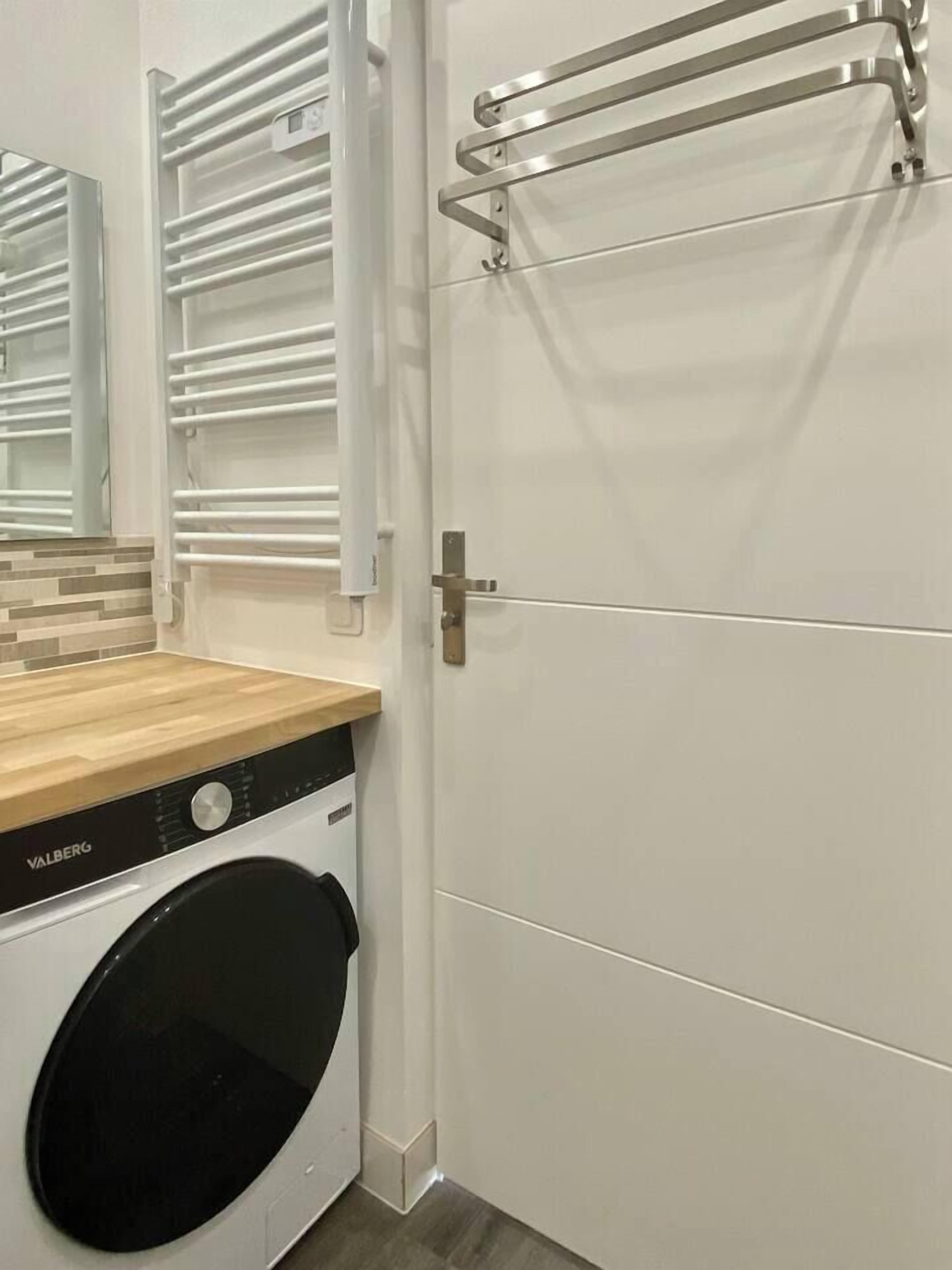 Une petite buanderie équipée d’un lave-linge, d’un étendoir et d’une porte avec une poignée.