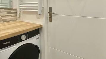 Une petite buanderie équipée d’un lave-linge, d’un étendoir et d’une porte avec une poignée.