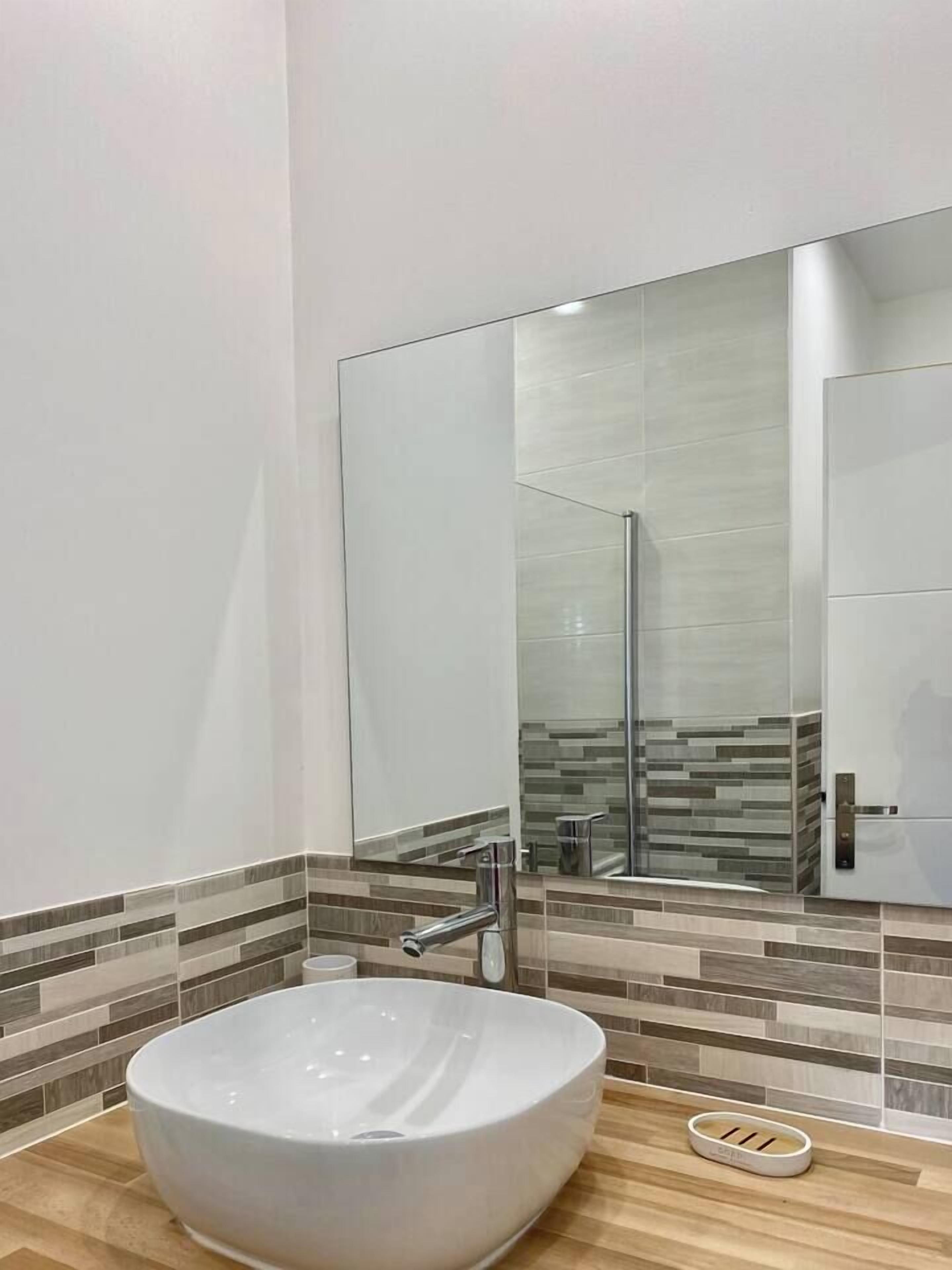 Une salle de bain moderne avec un grand lavabo sur pied blanc, un miroir et un mur recouvert de carreaux.