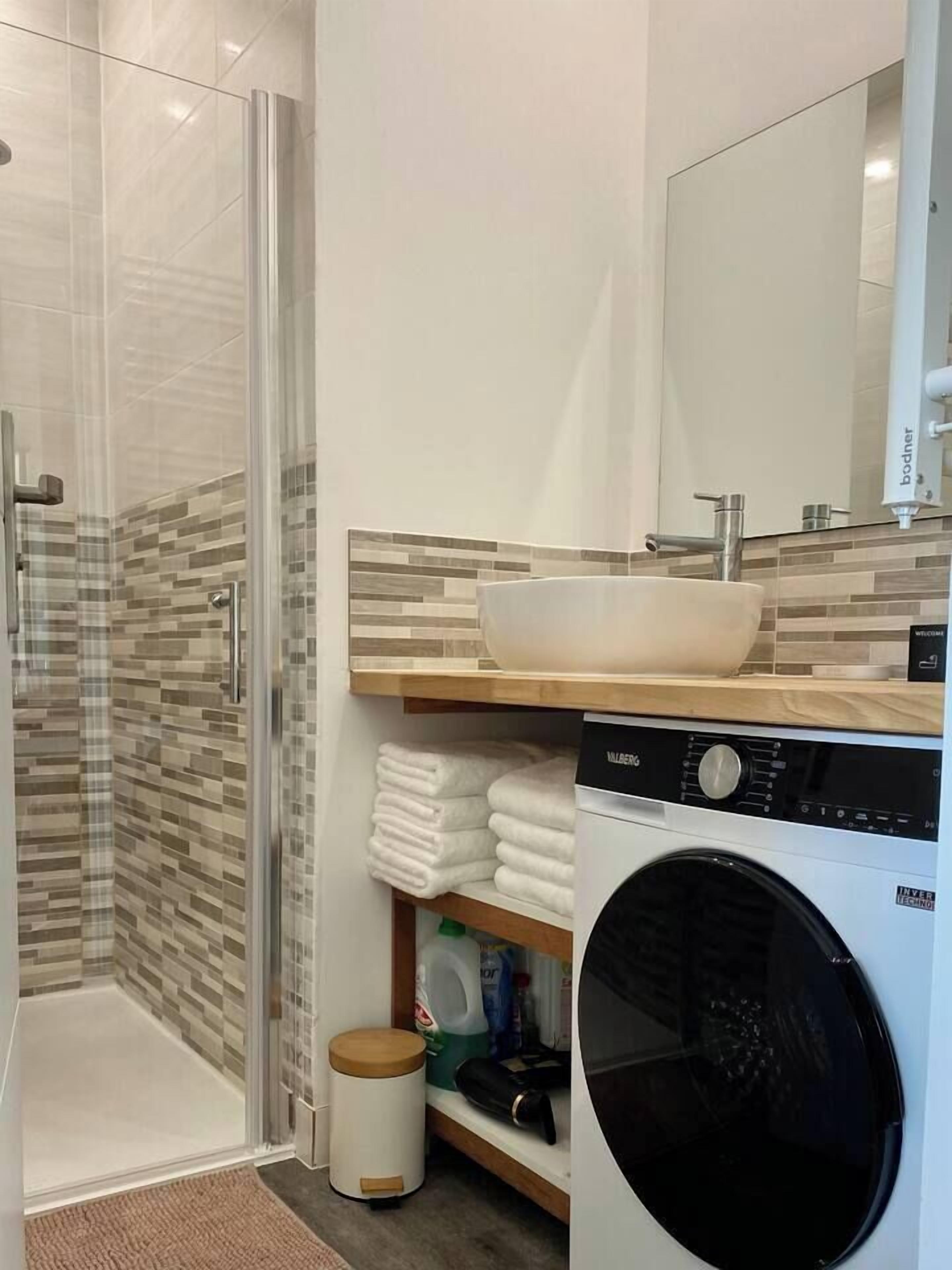 Ein modernes Badezimmer mit Duschkabine aus Glas, einem Holzbadezimmerzimmermöbel mit großem Waschbecken und einer Frontlader-Waschmaschine.