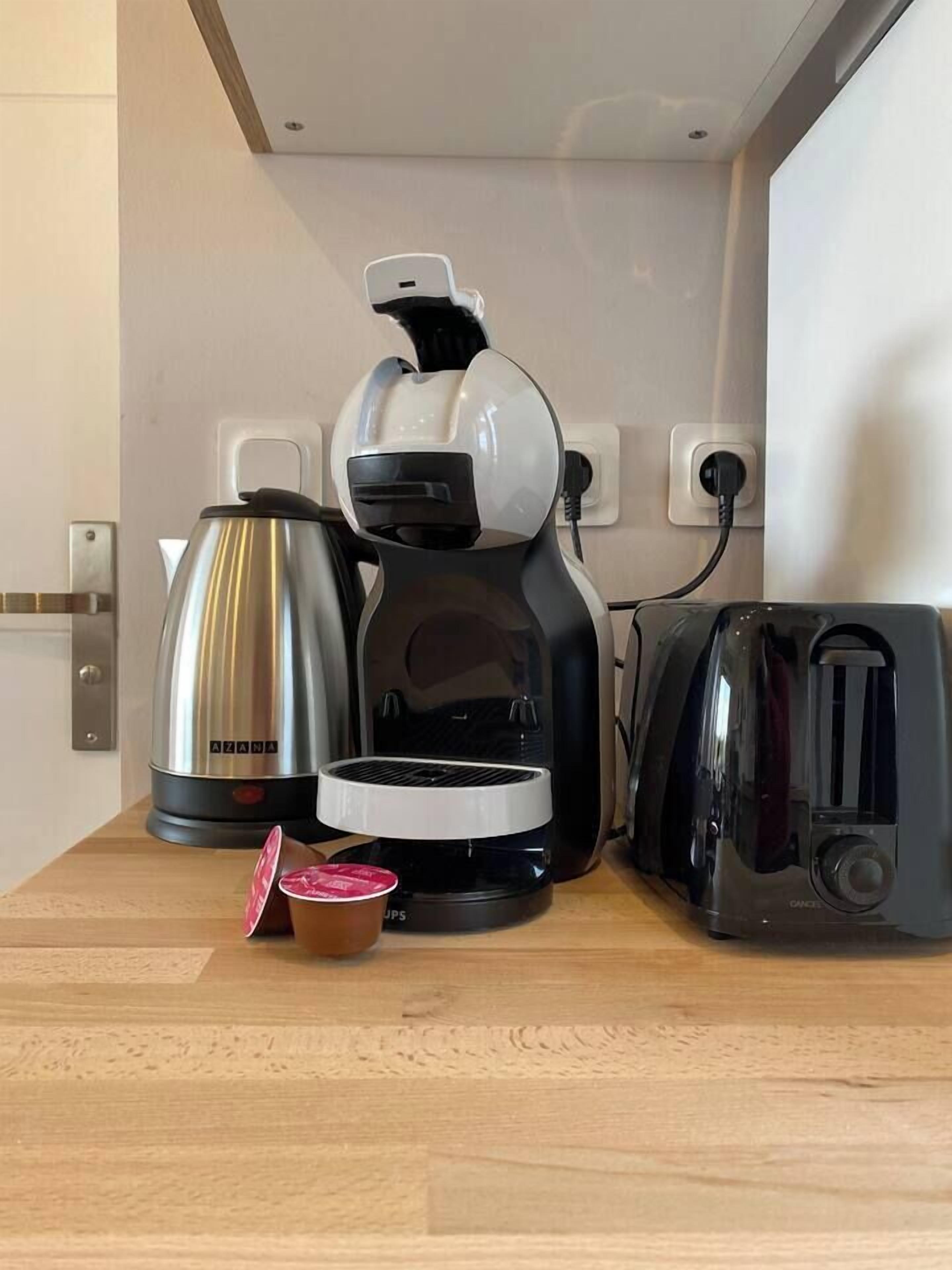 A kitchen with a coffee maker, a kettle, a toaster, and a cup of coffee on the counter.