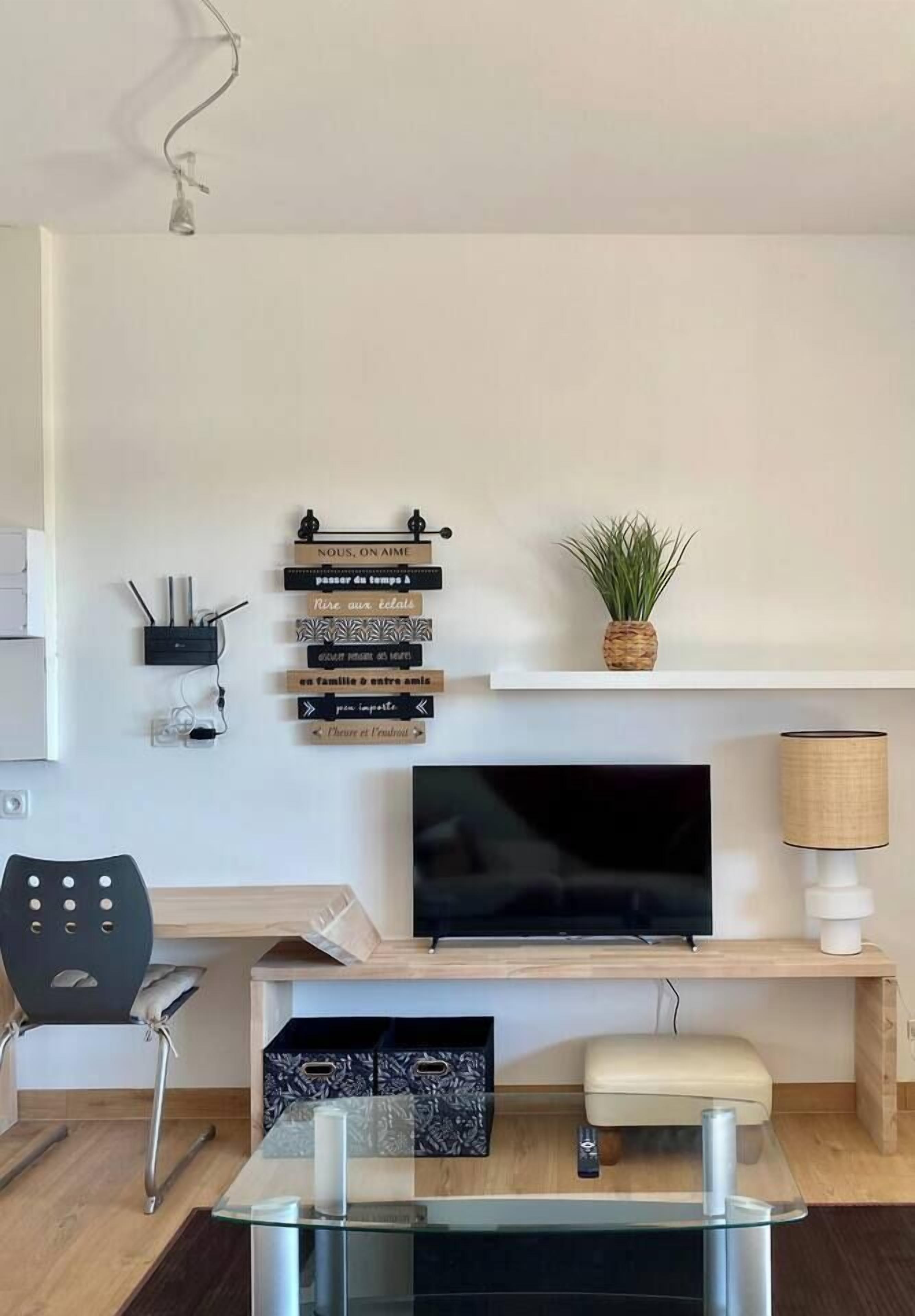 Ein modernes Wohnzimmer mit Flachbildfernseher, Glastisch, einer Couch und einem an der Wand befestigten Regal mit Dekorationselementen.