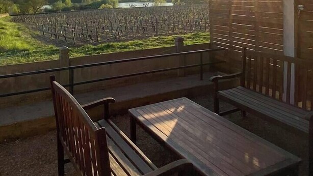 Une terrasse en bois avec un banc et une table, d’où l’on peut admirer un vignoble et une étendue d’eau.