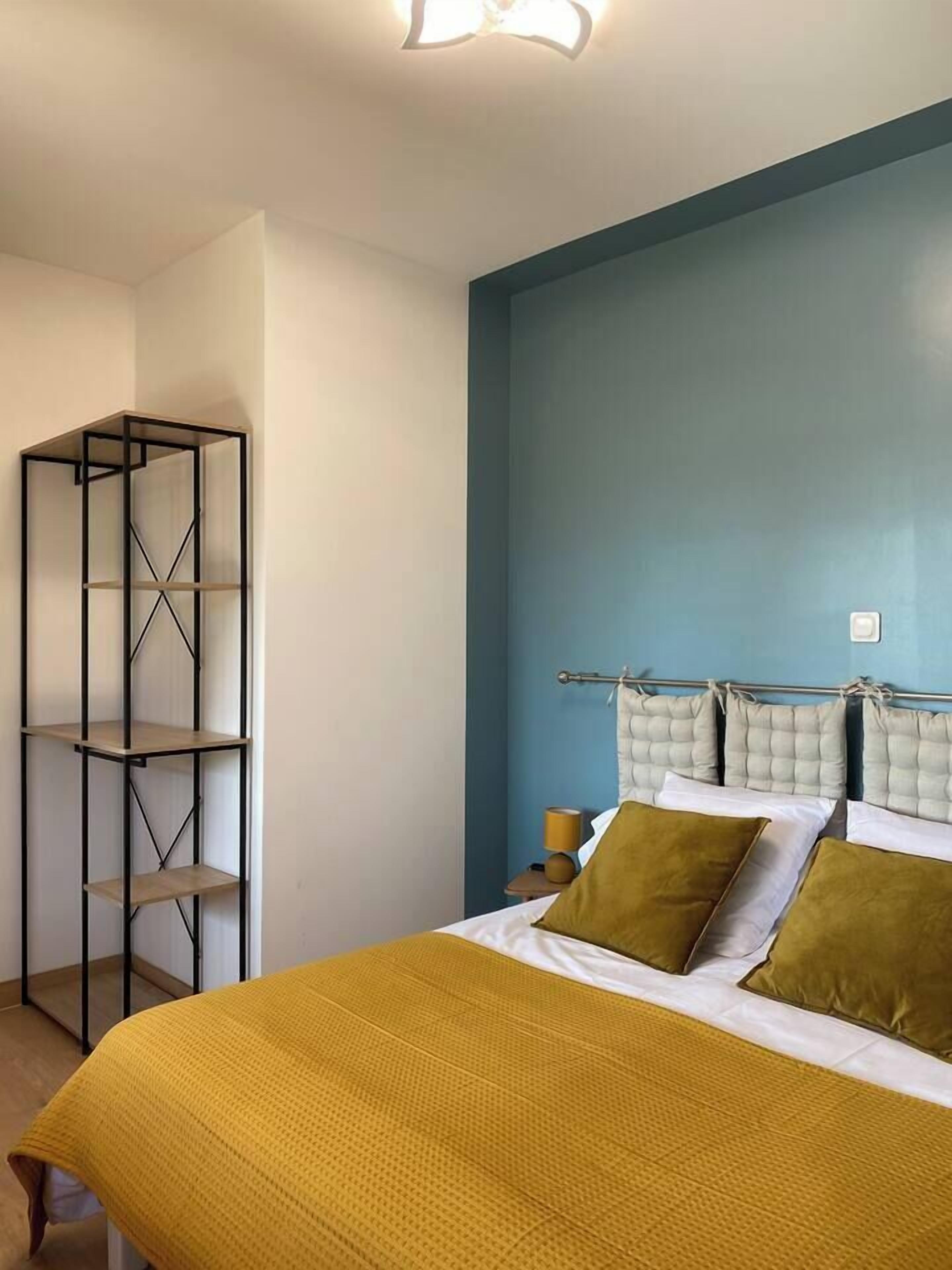 Ein Schlafzimmer mit einem Bett, einem Kopfteil mit Kissen, einem Nachttisch und einem an der Wand befestigten Metallregal.