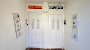 Un couloir avec deux portes blanches, un sol à motifs et des panneaux indicateurs au-dessus des portes.