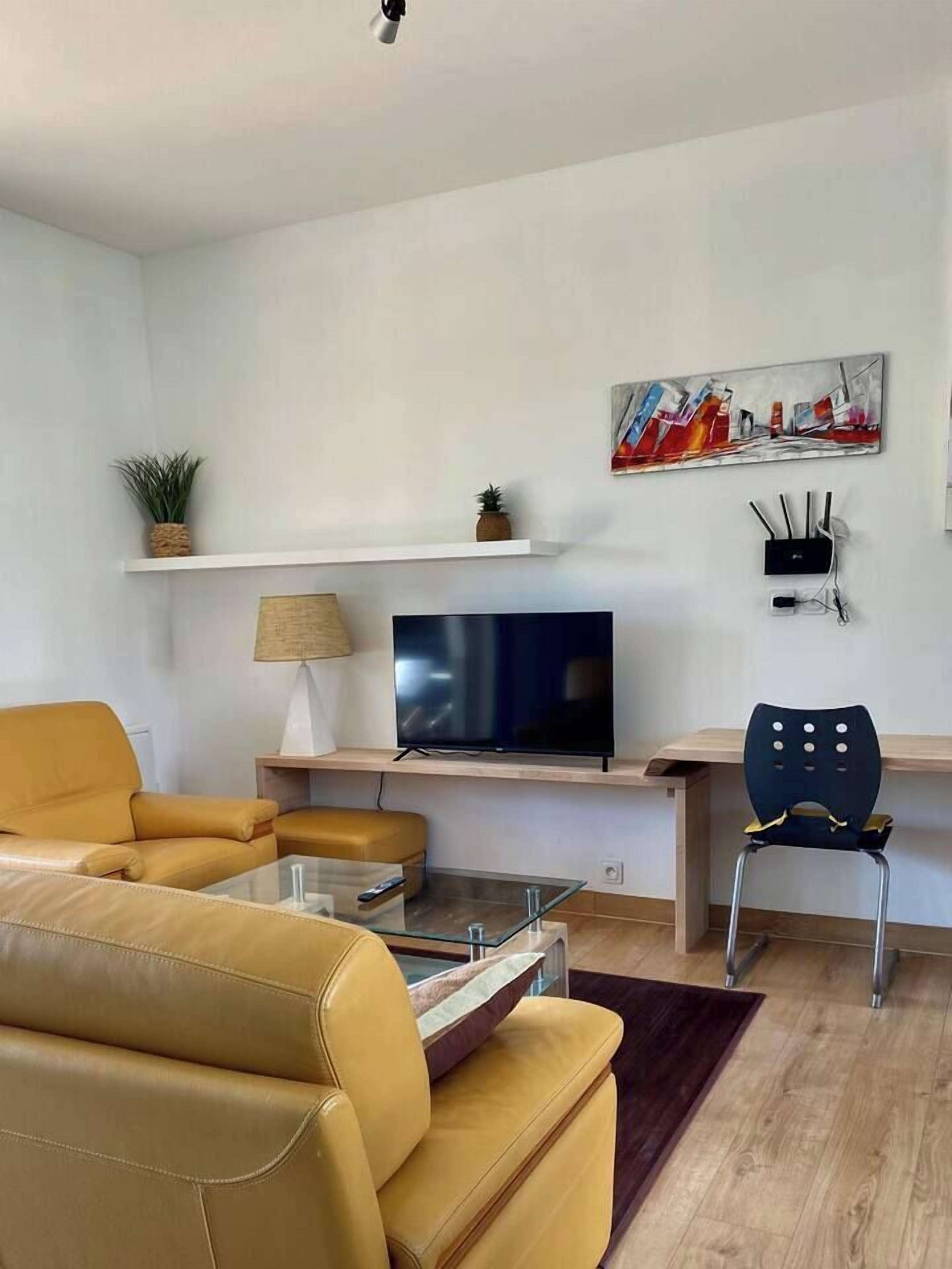 A modern living room with a sofa, a glass coffee table, a TV, a desk, and a chair.