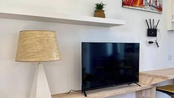 Ein modernes Wohnzimmer mit Fernseher auf einem Holzständer, einer Lampe, einer kleinen Pflanze und einem Gemälde an der Wand.