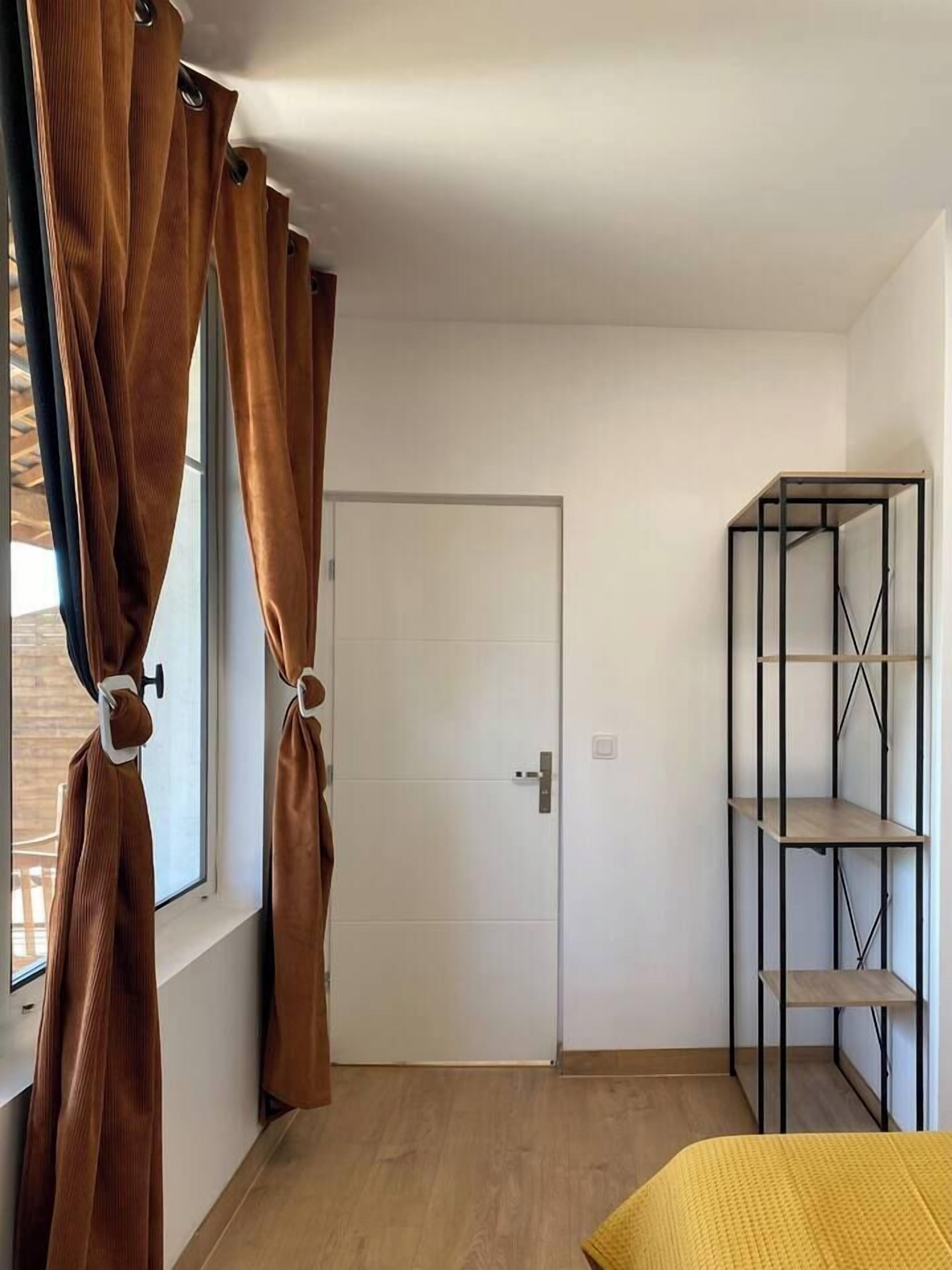 Habitació amb llit, armari, porta i finestra amb cortines.