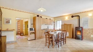 A cozy kitchen with wooden cabinets, a dining table, chairs, and a wood-burning stove.