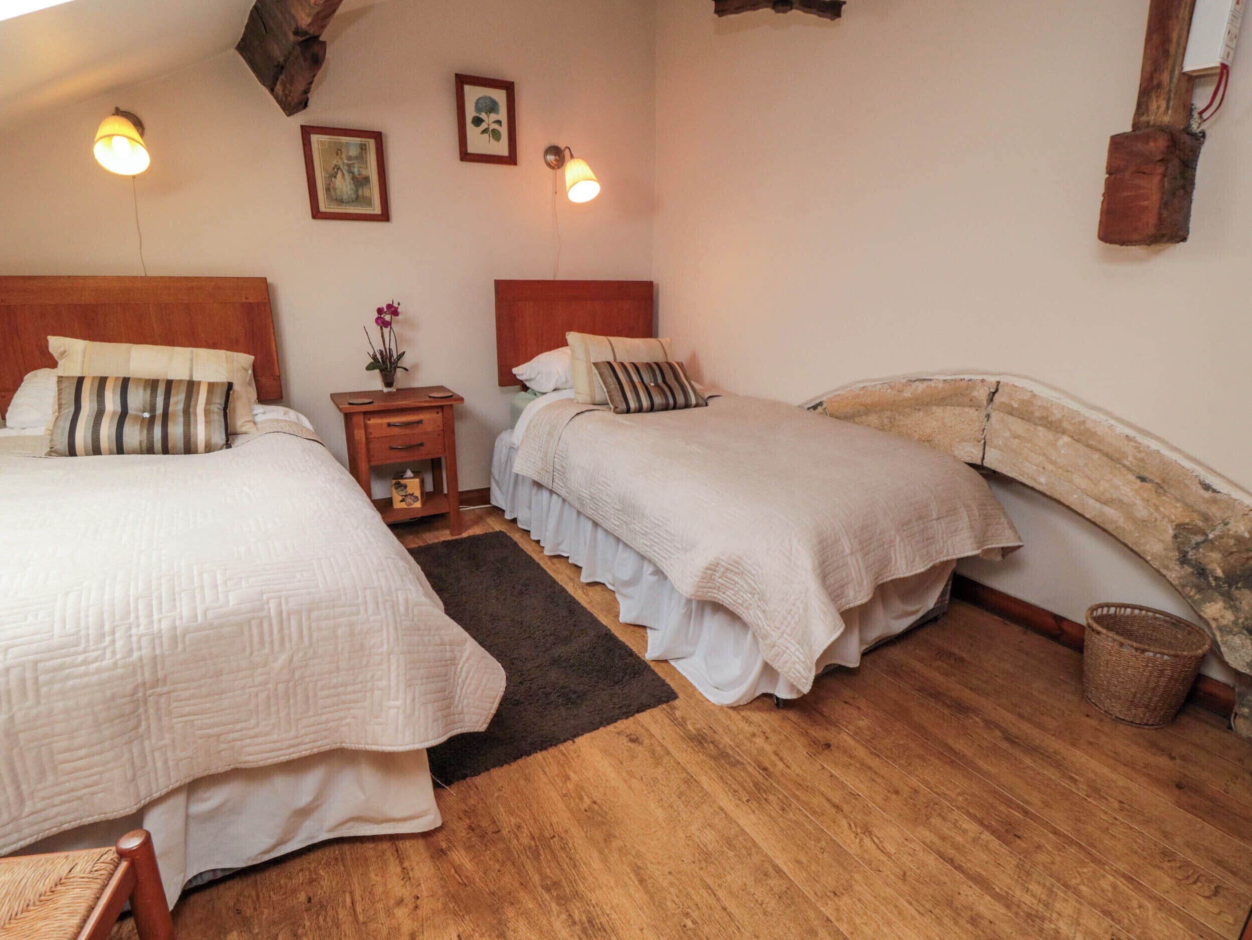 Ein gemütliches Schlafzimmer mit zwei Betten, Holz-Kopfteilen, einem kleinen Nachttisch mit einer Vase und einer rustikalen Wanddekoration.