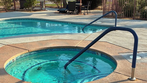 Una piscina con un trampolín y sillones de descanso al fondo.