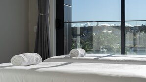 Quarto de hotel com uma janela grande, duas camas e duas toalhas dobradas sobre as camas.