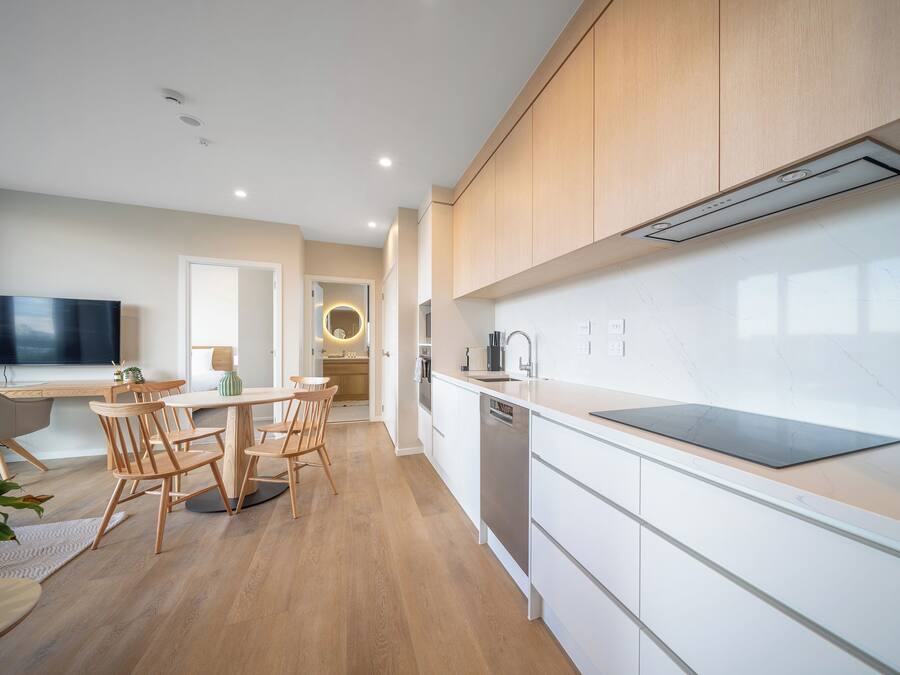 A modern kitchen with wooden cabinets, a dining area with a round table and chairs, and a built-in dishwasher.