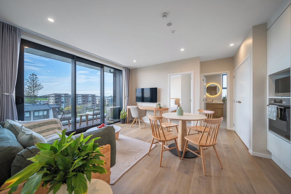 Un appartement moderne doté d’un grand balcon, d’un coin repas, d’une cuisine et d’un salon avec un canapé et une télévision.