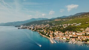 A coastal town with a marina, buildings with red-tiled roofs, and a mountainous backdrop.