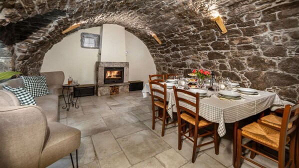 A stone-walled dining area with a fireplace, wooden chairs, and a table set for a meal.