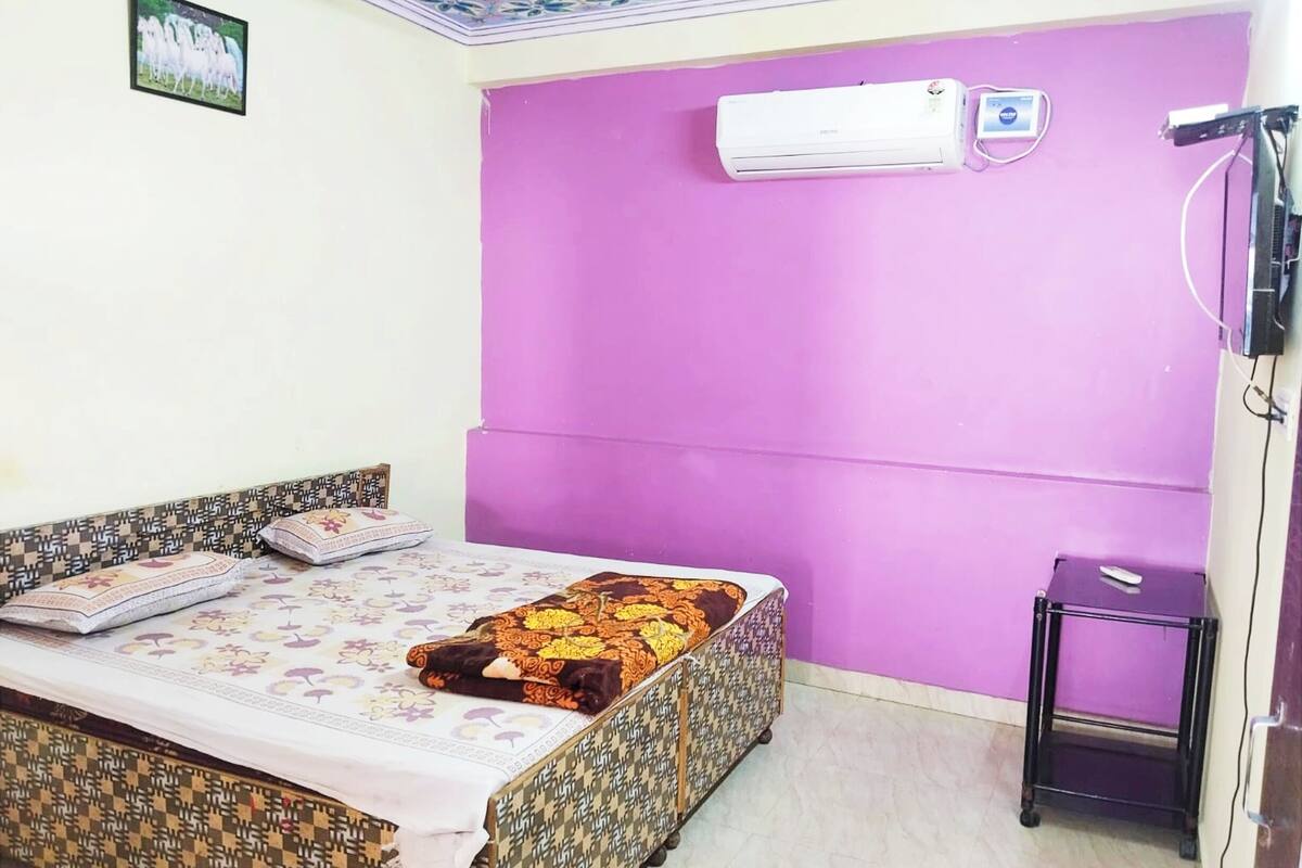 Une chambre avec un lit, un mur violet, un appareil de climatisation et une petite table.