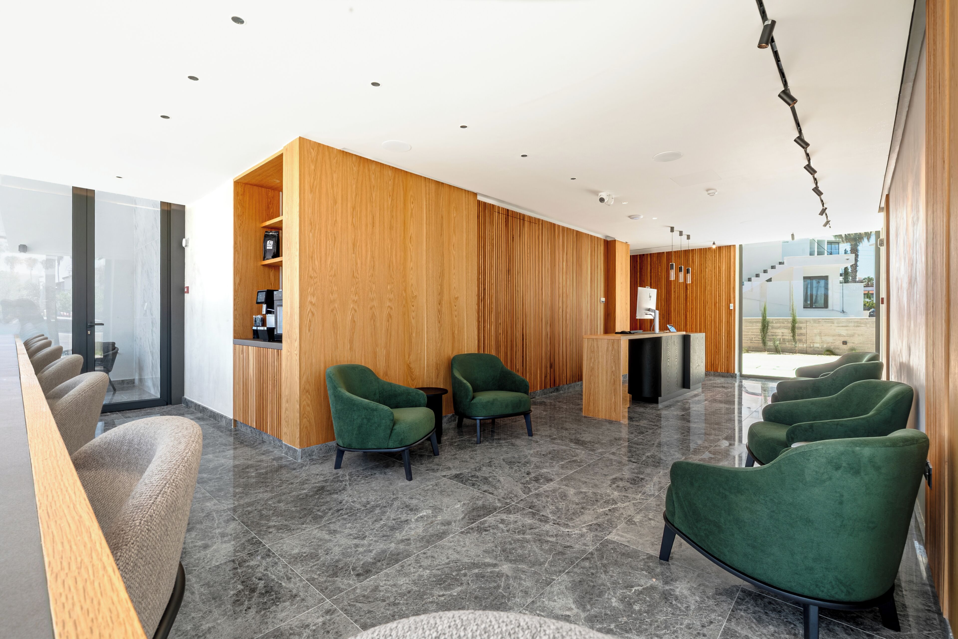 A modern reception area with wooden paneling, green upholstered chairs, and a reception desk.
