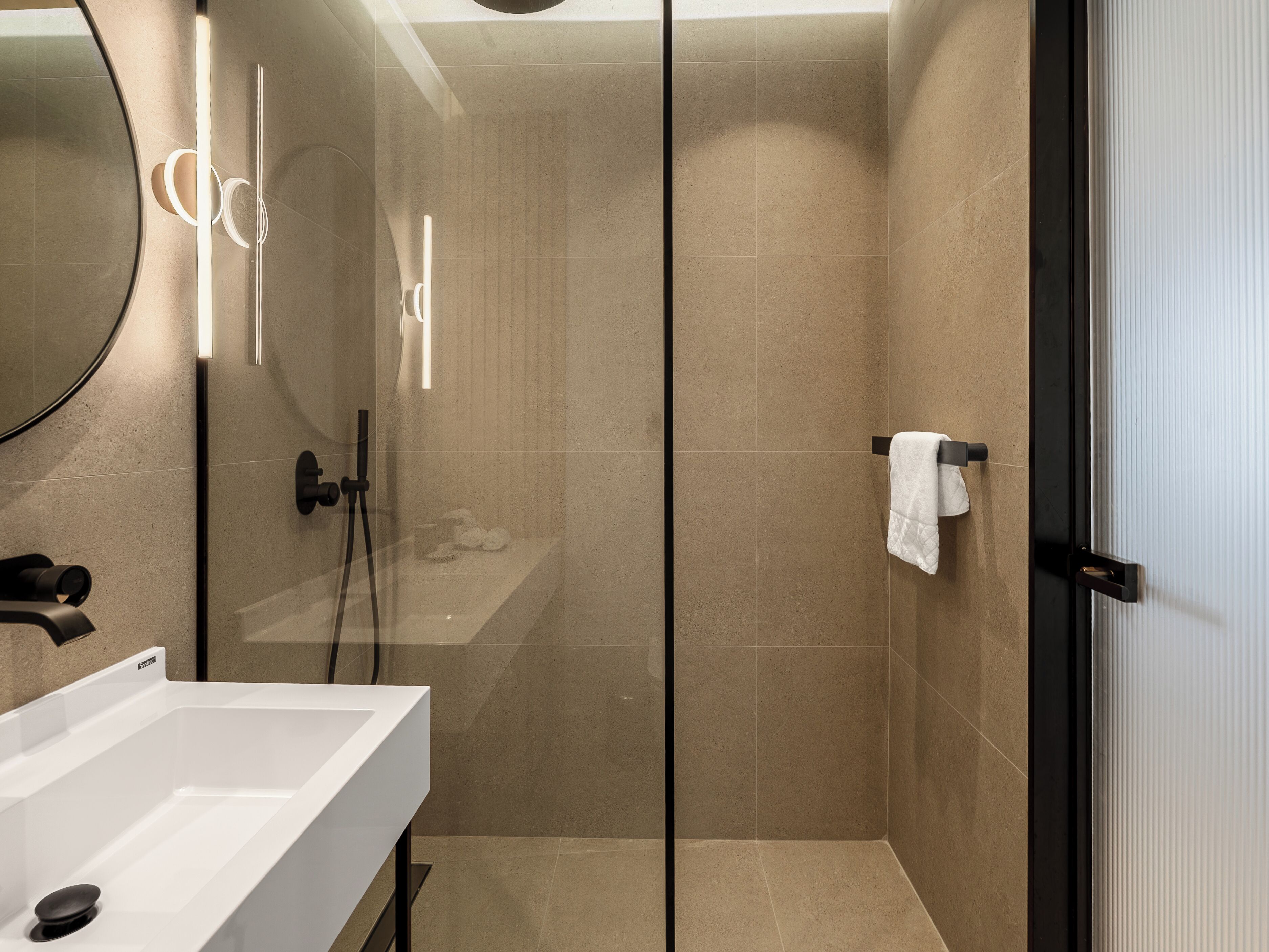 Un bagno moderno con cabina doccia in vetro, un lavandino bianco e un portasciugamani.