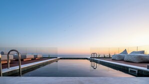 A rooftop pool with a clear view of the sea and a sunset.