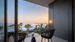A balcony with two chairs, a table, and a view of the sea and buildings.