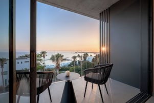Un balcón con dos sillas, una mesa y vistas al mar y edificios.