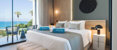 A modern bedroom with a large bed, a nightstand, a wall-mounted lamp, and a view of the ocean.