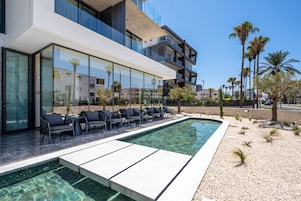 Un edificio moderno con piscina, mobiliario exterior y palmeras.